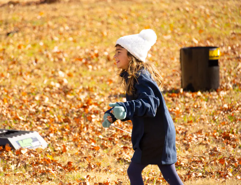 Girl in a white knit hat running across autumn leaves at Lake Hudson Resort